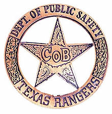 A bronze circle star badge with the words "Dept. of Public Safety" across the top of the circle and the words "Texas Rangers" across the bottom. There are two branches going up the sides of the circle. In the middle of the star is the words "Co B" and there are decorative swirls in the star.