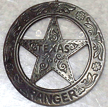 A heavily ornamented silver circle star badge with the word "Texas" in the center of the star and the word "Ranger" on the bottom of the circle.