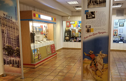 A brightly colored exhibit gallery with three cases visible and two large printed floor to ceiling panels.