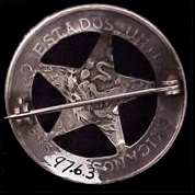 The back of a silver circle star badge with the vague imprint of a Mexican coin visible.