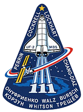 A space shuttle patch with the shuttle taking off in the center, a satellite orbiting the shuttle, and the names of the astronauts.