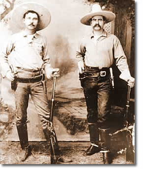 Two men dressed in 1890s Ranger gear posing for a photograph in wide brimmed hats carrying their rifles.