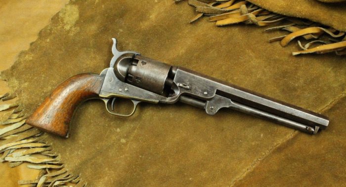 A silver metal pistol with a wooden butt on top of a fringed suede background.