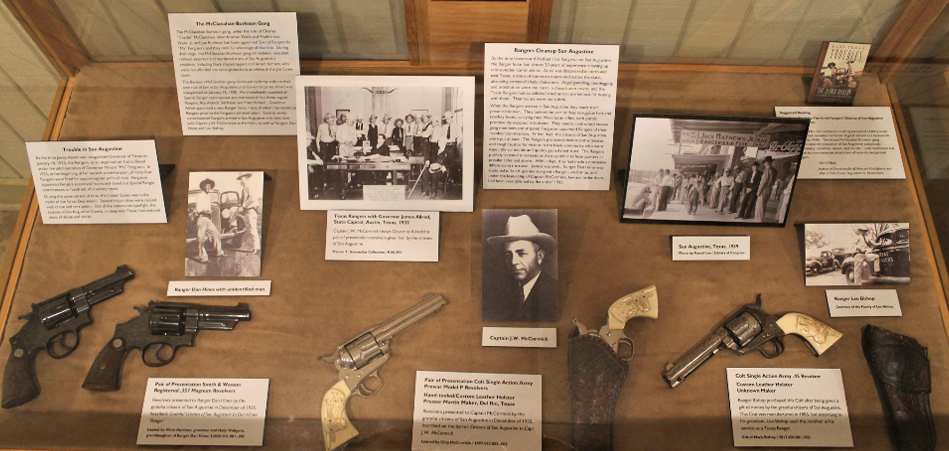 An exhibit case with photographs, labels, and various pistols.