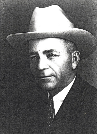 A man in a dark suit with a dark tie in a white cowboy hat.