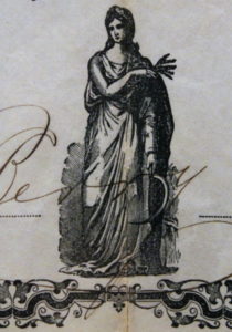 A black inked woman in a robe with a scythe and wheat in her hands. There is a decorative border below her and the edge of writing across her.