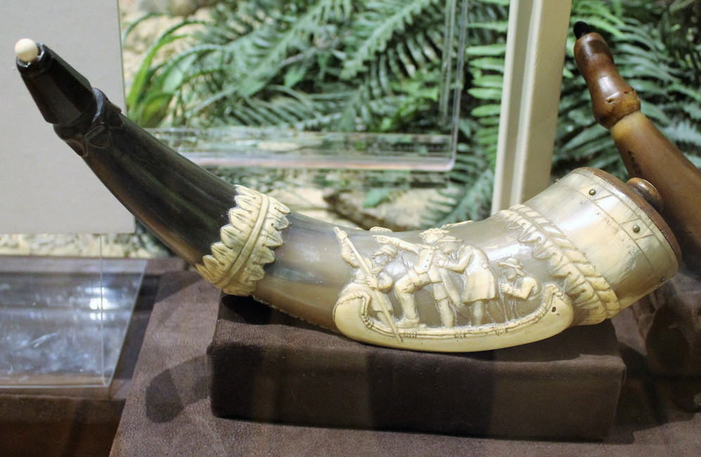 A powder horn with a carving of men standing in a boat.