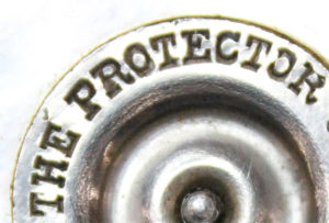 A zoomed in picture on a round metal circle that reads "The Protector"