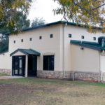 A white building with a green roof and a tan rock rim along the bottom.